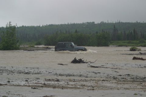2003 Jeep TJ - A Jeep TJ navigates through a flooded area, kicking up water as it moves.