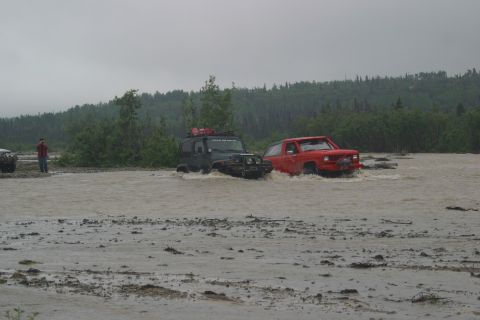 2003 Jeep TJ - Two off-road vehicles navigate a flooded terrain with trees in the background.