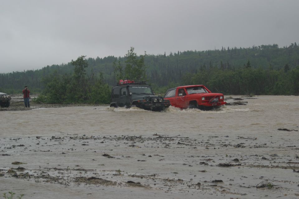 Green 2003 Jeep TJ and red SUV driving through muddy water, front view