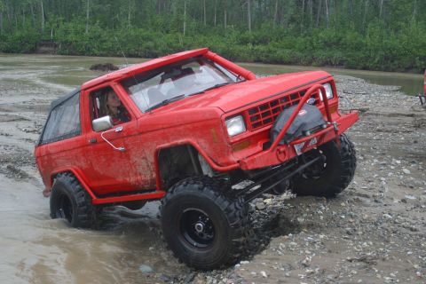 2003 Jeep TJ - This red off-road SUV navigates a rocky stream bed, its capabilities.