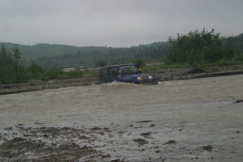 2003 Jeep TJ - Blue 2003 Jeep TJ navigating a muddy river crossing under an overcast sky.
