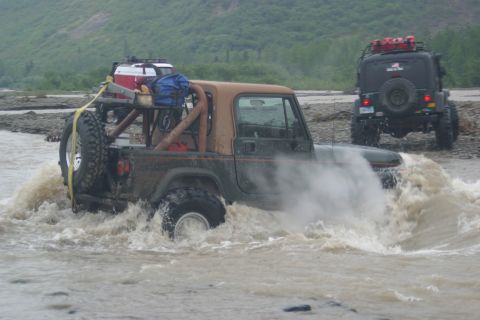 2003 Jeep TJ - A green 2003 Jeep TJ with a brown soft top navigates a shallow river, with another Jeep following behind.