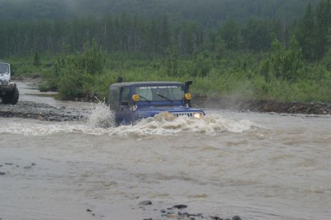 2003 Jeep TJ - Two Jeeps navigate a river crossing with trees and brush in the background.