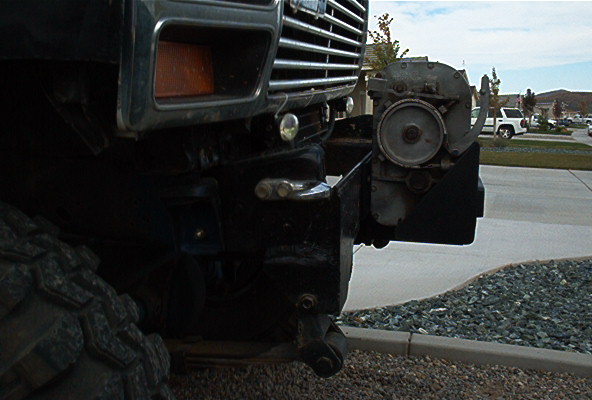 Front bumper with winch and grille of a dark-colored vehicle, with a white SUV in the background