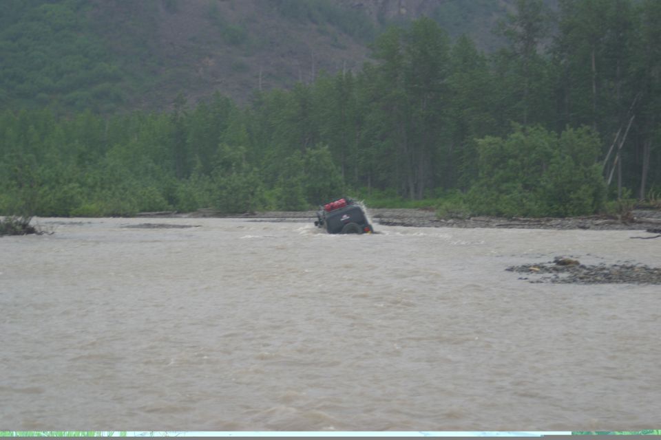 Dark SUV driving through a river with red bags on top