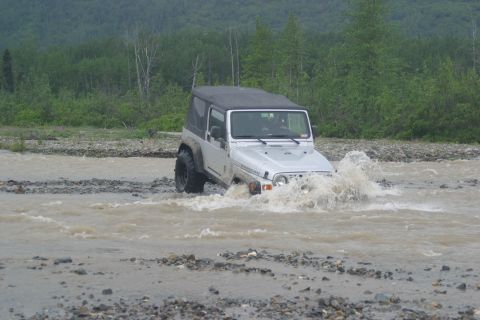 2003 Jeep TJ - A Jeep Wrangler navigates a rocky riverbed, kicking up water.