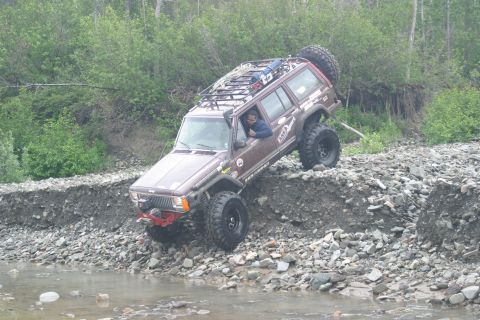 2003 Jeep TJ - A modified Jeep Cherokee XJ is shown off-roading on a steep, rocky embankment.