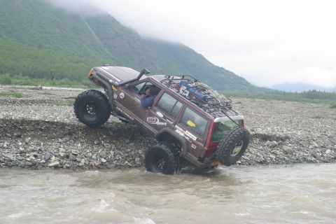 2003 Jeep TJ - An off-road SUV navigates a rocky riverbed, its tires partially submerged in the water.