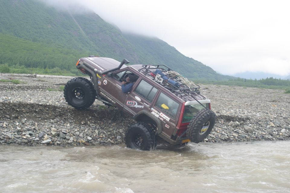 Brown off-road SUV with roof rack and snorkel driving through shallow water