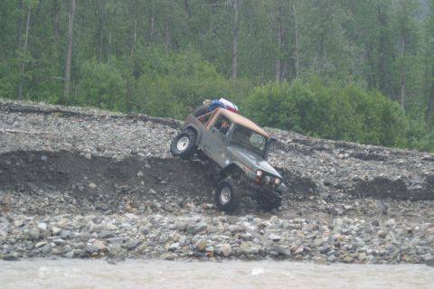 2003 Jeep TJ - Jeep TJ tackles a challenging rocky slope near a river, loaded with gear on the roof.