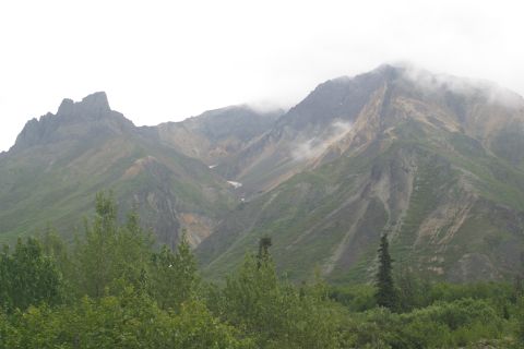 2003 Jeep TJ - A vast mountain range is shrouded in clouds, with lush green trees in the foreground.
