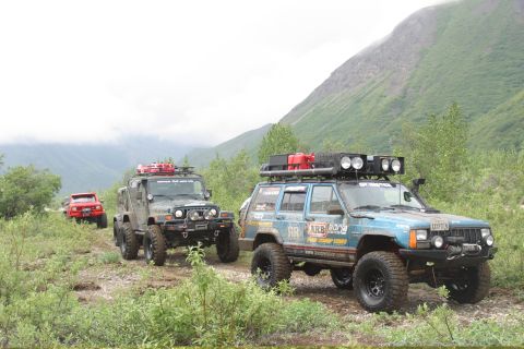 2003 Jeep TJ - Three off-road vehicles, including a blue Jeep Cherokee and a green Jeep Wrangler, travel on a dirt path through a mountainous, vegetated l…
