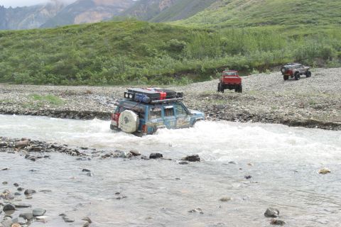 2003 Jeep TJ - Off-road vehicles navigate a river in a mountainous, vegetated area.