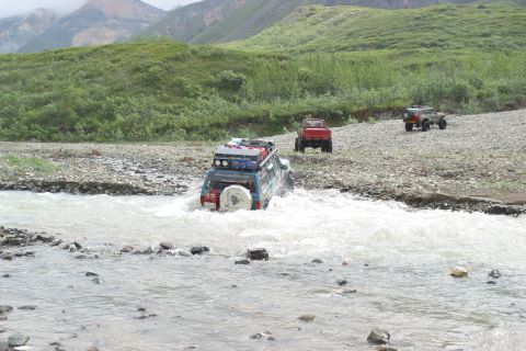 2003 Jeep TJ - Multiple off-road vehicles navigate a rocky riverbed in a mountainous, vegetated landscape.