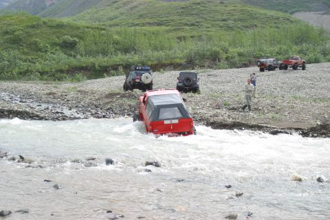 2003 Jeep TJ - Several off-road vehicles navigate a rocky stream bed in a scenic, mountainous area.