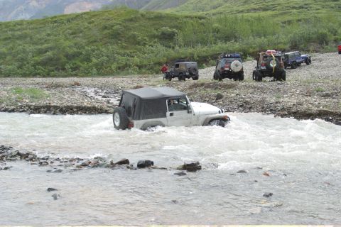 2003 Jeep TJ - Several Jeep Wranglers navigate a shallow, rocky river in a natural landscape.