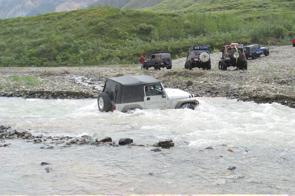 White Jeep TJ crossing a rocky river with other Jeeps on the bank