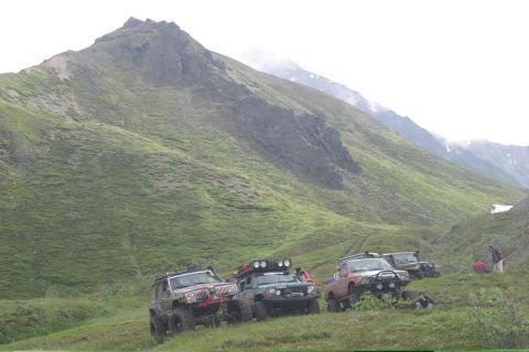 2003 Jeep TJ - Off-road vehicles are parked on a grassy mountainside under a cloudy sky.