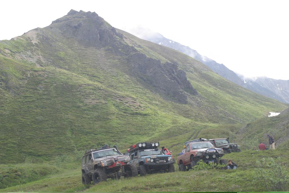 Four-wheel drive vehicles parked on a grassy slope with a mountain in the background