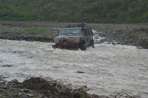 2003 Jeep TJ - A Jeep Cherokee XJ navigates a rocky river crossing with a roof rack and winch visible.