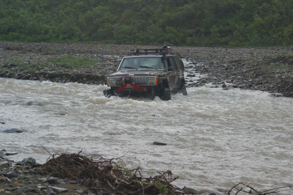Brown Jeep Cherokee XJ driving through a river, front view. It has a roof rack and a winch