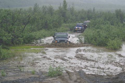 2003 Jeep TJ - A convoy of Jeeps navigates a muddy trail, with the lead vehicle splashing through deep water and mud.