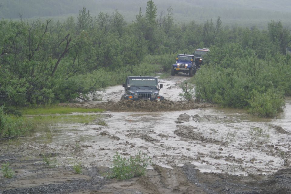 Dark Jeep Wrangler driving through mud, with two other Jeeps behind it