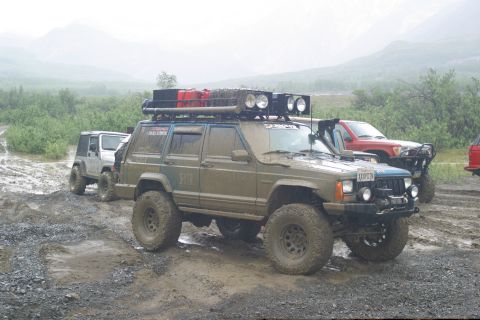 2003 Jeep TJ - Several off-road vehicles, including a mud-splattered Jeep Cherokee XJ, navigate a wet and rocky terrain.