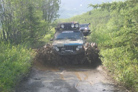 2003 Jeep TJ - A teal Jeep Cherokee XJ navigates a muddy trail, kicking up spray, with another Jeep following behind.