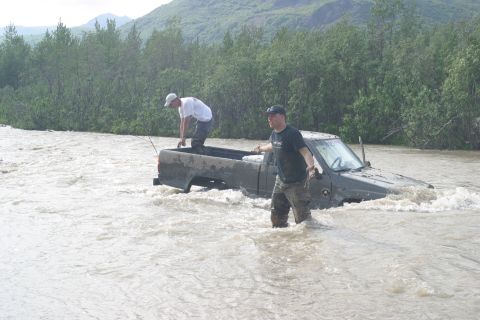 2003 Jeep TJ - Two men navigate a flooded river next to a partially submerged pickup truck.