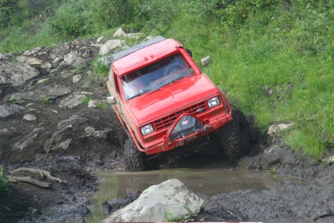 2003 Jeep TJ - This red SUV is tackling a challenging off-road course with mud and rocks.