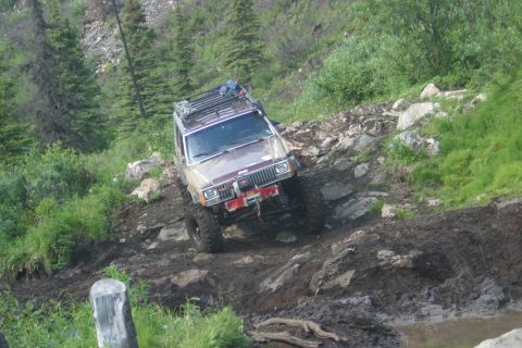 2003 Jeep TJ - A modified Jeep Cherokee XJ tackles a challenging off-road course with steep inclines and muddy terrain.