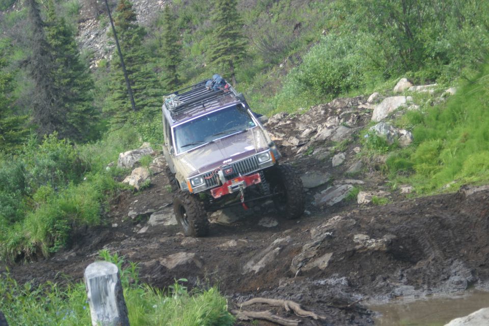 Brown Jeep Cherokee XJ with a roof rack and winch navigates a muddy, rocky trail