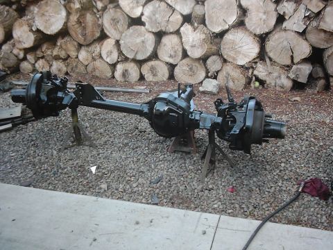 1978 Ford Bronco - Axle assemblies are set up on jack stands outdoors, with a woodpile behind them.
