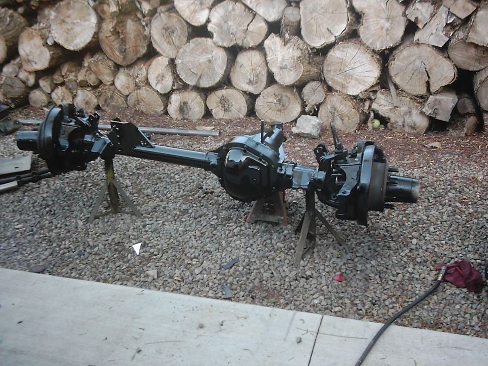 Front and rear axle assemblies on jack stands, with a pile of logs in the background