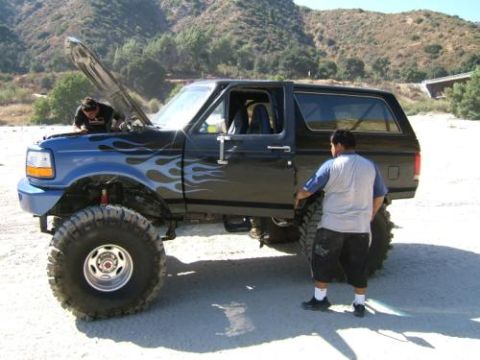 1991 Ford Bronco - A lifted black Ford Bronco with custom flame decals is being worked on outdoors.