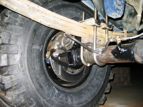 1985 Ford Bronco - Close-up view of the rear axle and suspension system of a vehicle, showing the tire, brake assembly, and leaf springs.