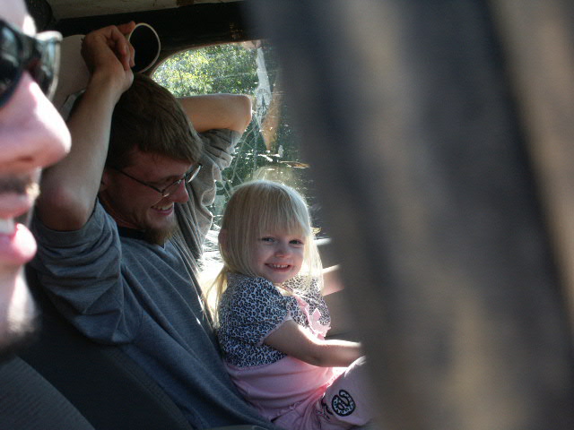 Man in glasses and a young blonde girl smiling inside a vehicle, seen through the open door
