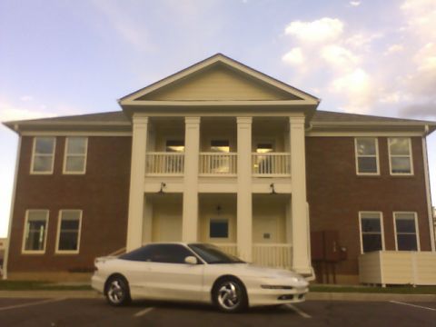 1996 Ford Probe - A white 1996 Ford Probe is parked in front of a large brick building with a white facade and columns.