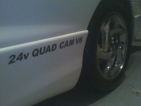 1996 Ford Probe - Side view of a white car with a '24v QUAD CAM V6' decal and a chrome wheel is visible.