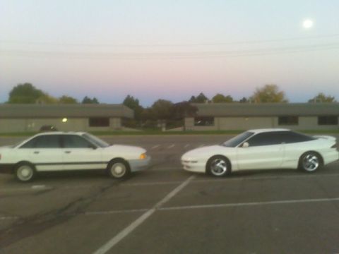 1996 Ford Probe - Two white cars are parked in a lot during twilight with a building in the background.