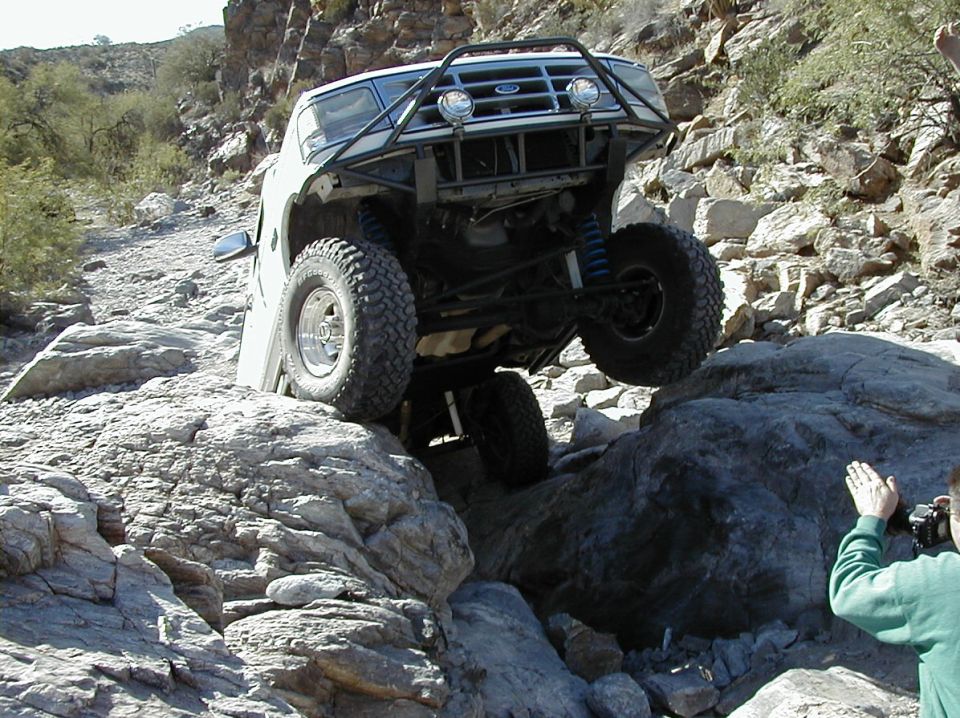 White lifted Ford Bronco pitched up on boulders showing front axle and blue coilovers