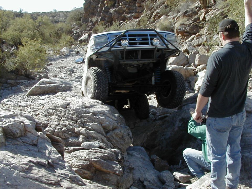 White Ford Bronco flexing over a desert rock ledge with exposed front axle