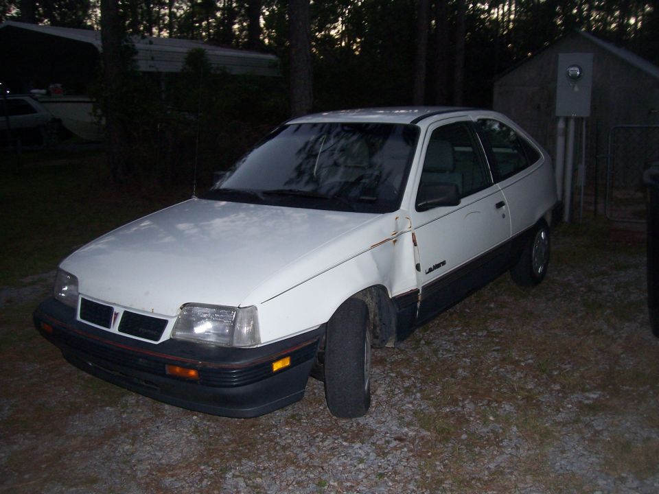 White hatchback car with damage to the front fender and rust on the door seam