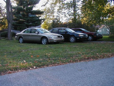 1990 Ford Taurus - Three sedans are parked on the grass in front of a house.