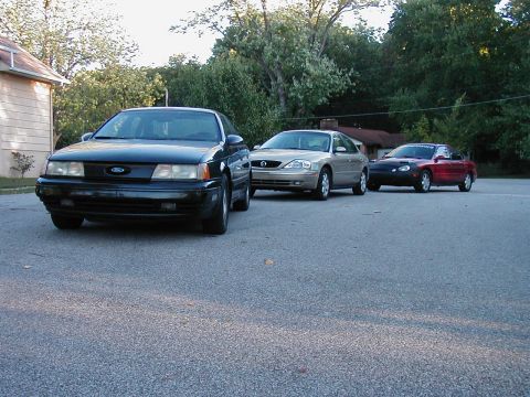 1990 Ford Taurus - Three cars are parked in a lot, led by a 1990 Ford Taurus.