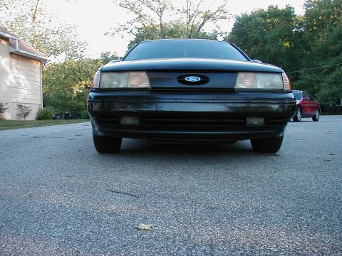1990 Ford Taurus - Frontal view of a black 1990 Ford Taurus, with a red vehicle in the background.