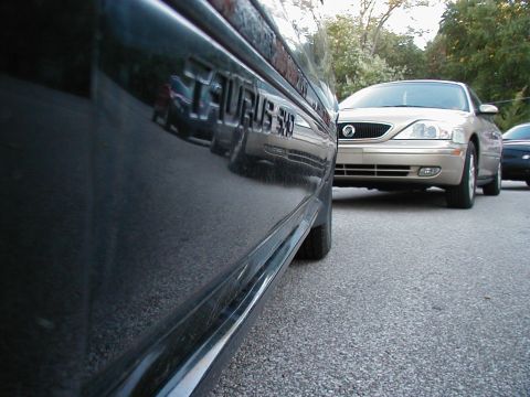 1990 Ford Taurus - A close-up view of the 'Taurus SHO' emblem on a vehicle, with other cars parked nearby.