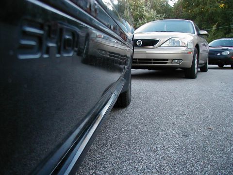 1990 Ford Taurus - A dark-colored Ford Taurus SHO is parked on an asphalt surface, with other vehicles visible in the background.