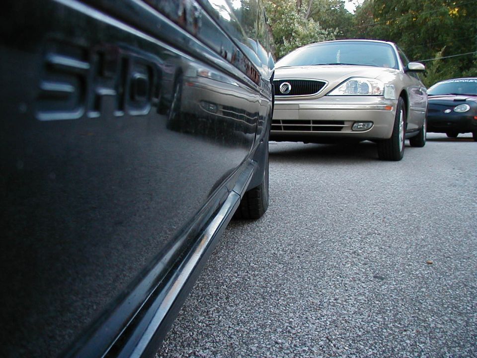 Black Ford Taurus SHO side profile, parked on asphalt, with a gold Mercury Sable and a dark car behind it